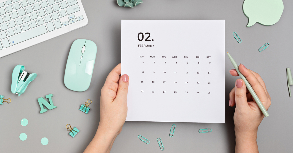 mani che reggono calendario su una scrivania con una tastiera e un mouse